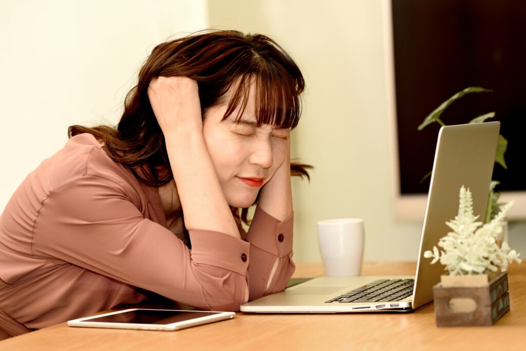 頭を抱えて悩む女性、ノートパソコン
