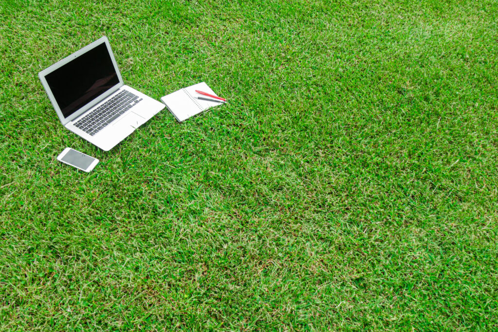 芝生の上のノートPCとスマホ